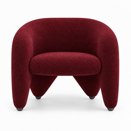 Faye armchair front view showing wrap-around shell and splayed sculptural legs in burgundy boucle